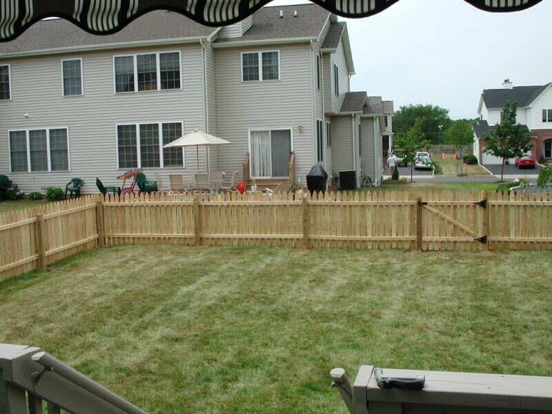 A backyard with a wooden fence and a house in the background