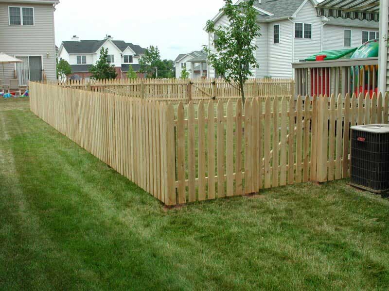 A wooden picket fence is in the middle of a lush green yard.