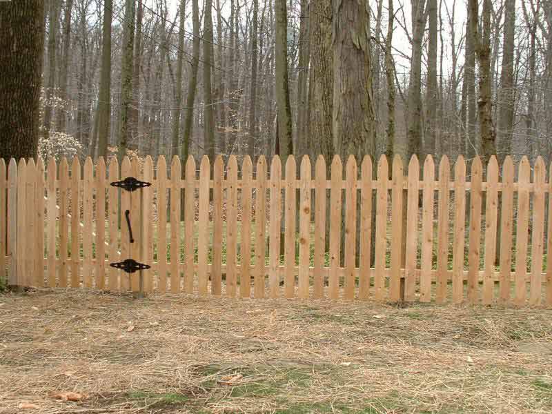 A wooden picket fence with a gate in the middle of the woods