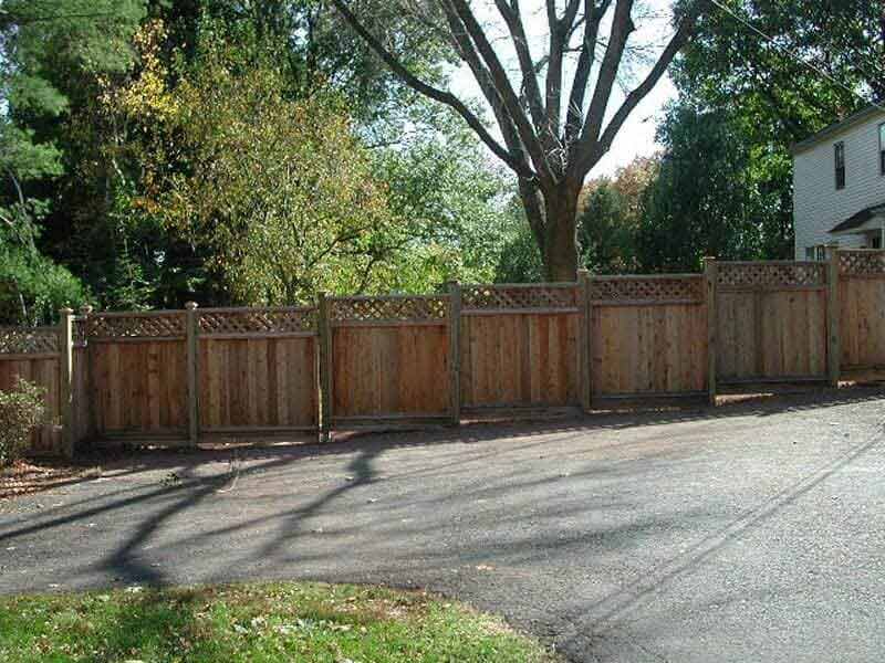 A wooden fence surrounds a driveway with trees in the background