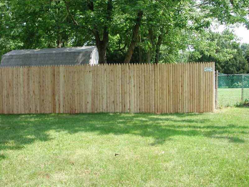 A wooden fence is in the middle of a lush green field.