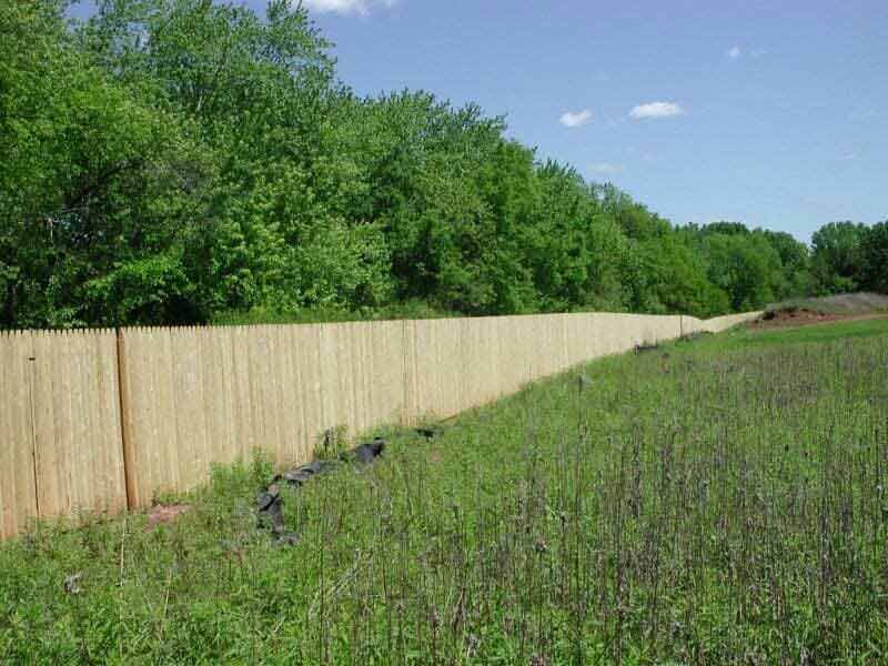 A wooden fence surrounds a grassy field with trees in the background.