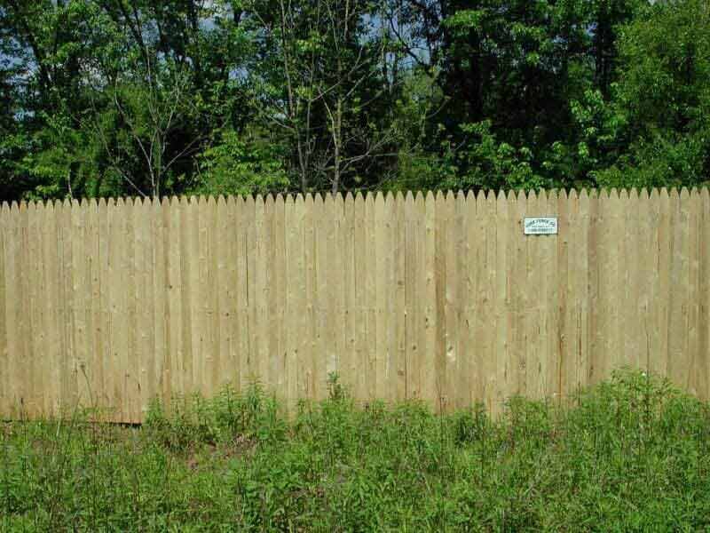 A wooden fence surrounds a grassy field with trees in the background