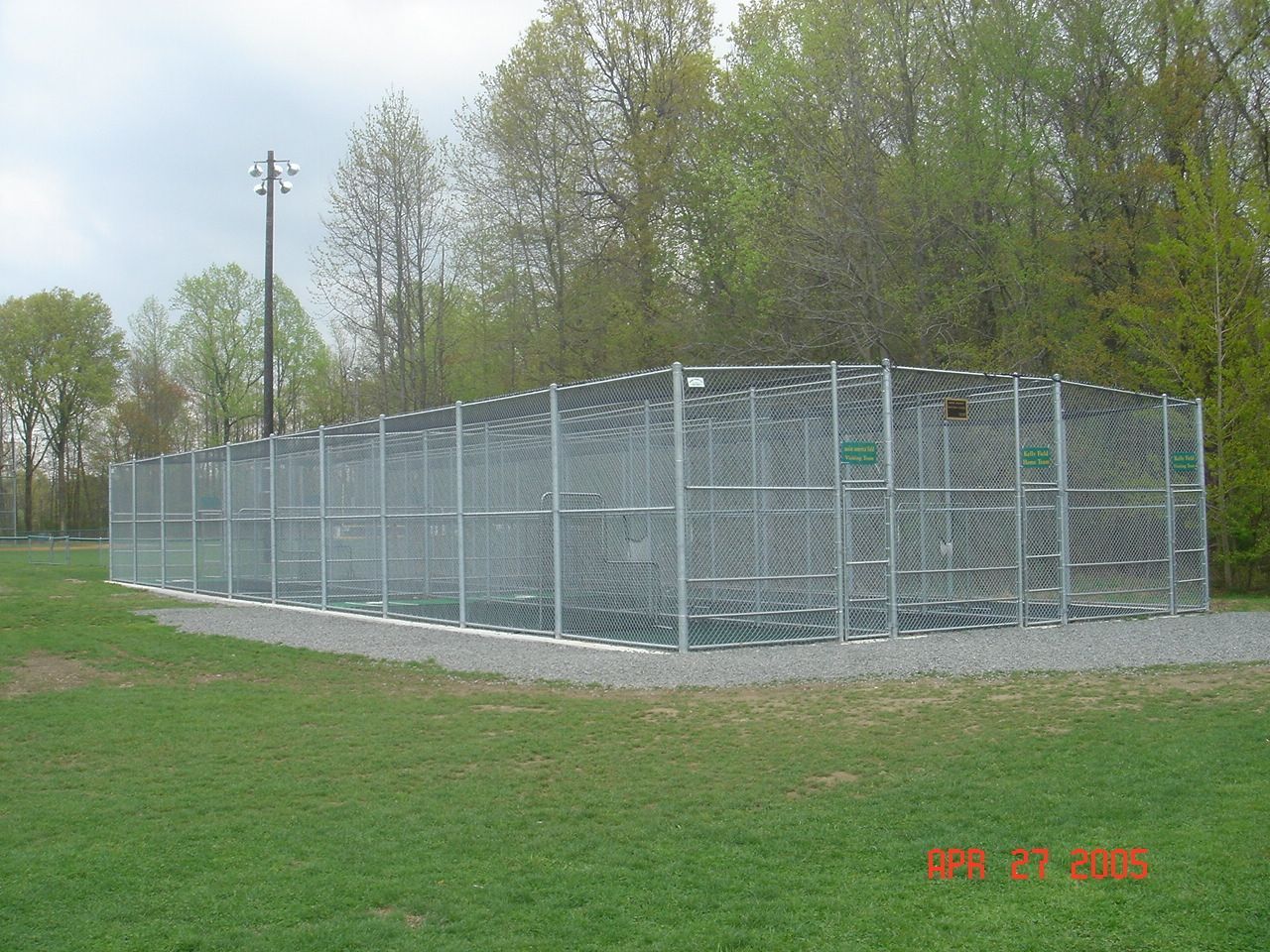 A large metal fence surrounds a baseball field in a park.