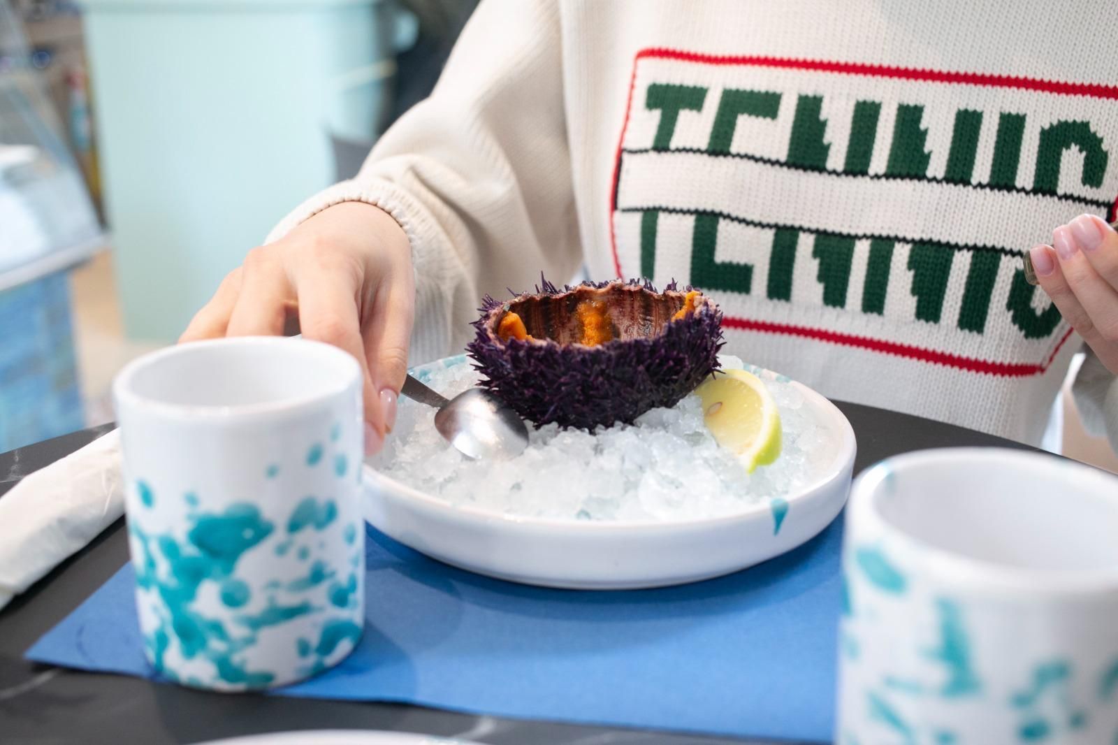 Piatto di frutti di mare con limoni e arance su un tavolo; bottiglie e bicchiere di vino sullo sfondo.