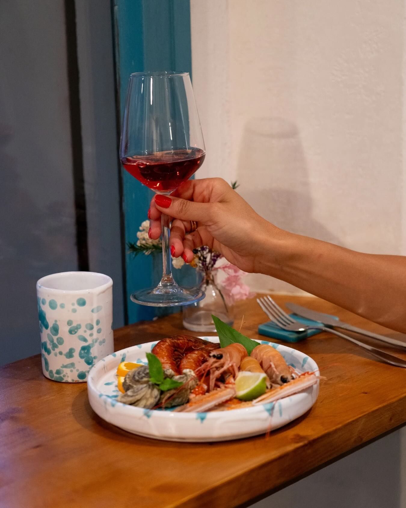 Piatto di frutti di mare con limoni e arance su un tavolo; bottiglie e bicchiere di vino sullo sfondo.