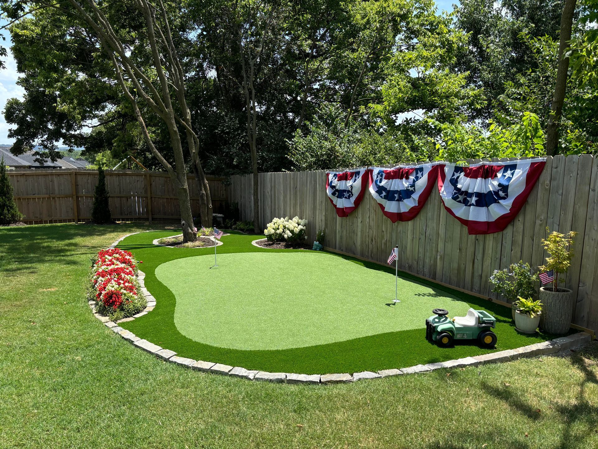 Backyard putting green with red, white, and blue bunting, a toy tractor, and colorful flowers.