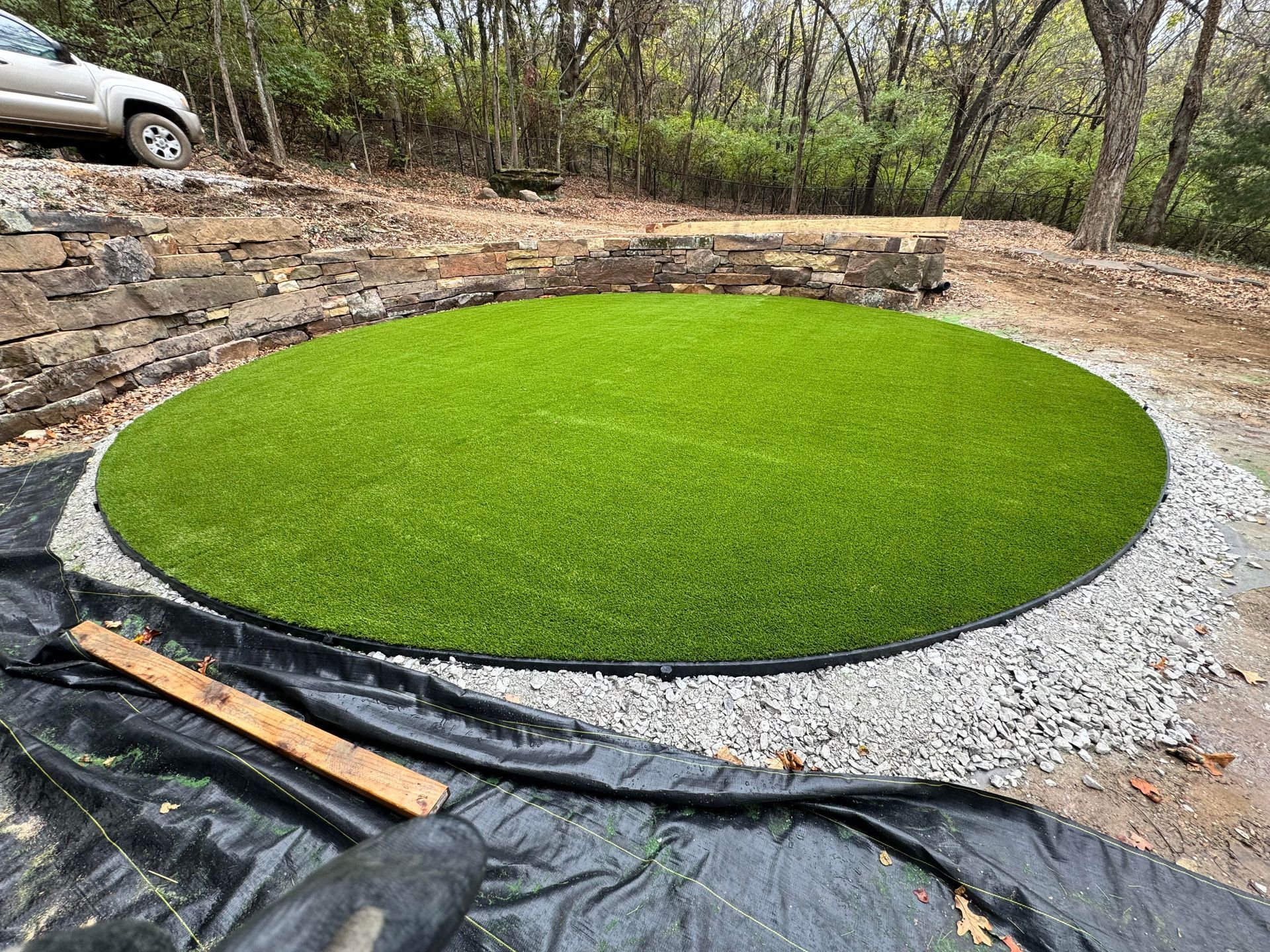 Circular patch of bright green artificial turf surrounded by gravel, set into a hillside.