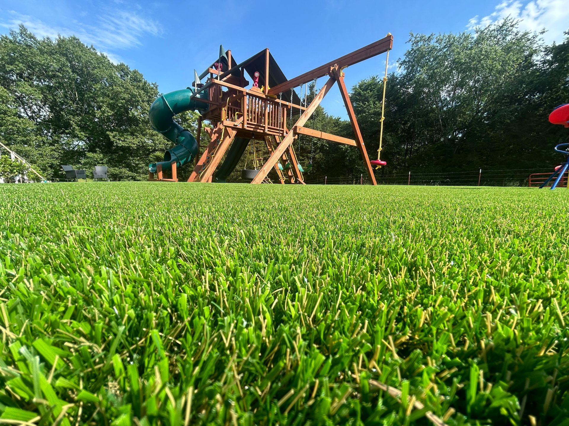 Playground on lush green lawn under a blue sky. Wooden structure with slide and swings.