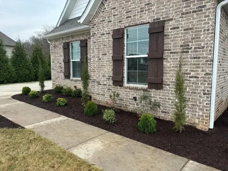 A brick house with brown shutters and a sidewalk in front of it.