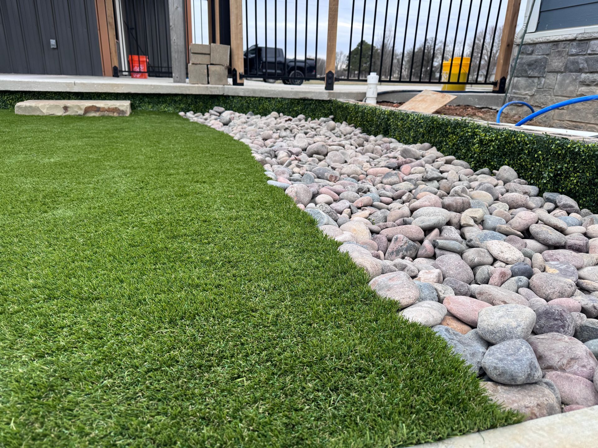 Artificial turf and river rock landscape bordering a building; green and gray tones.