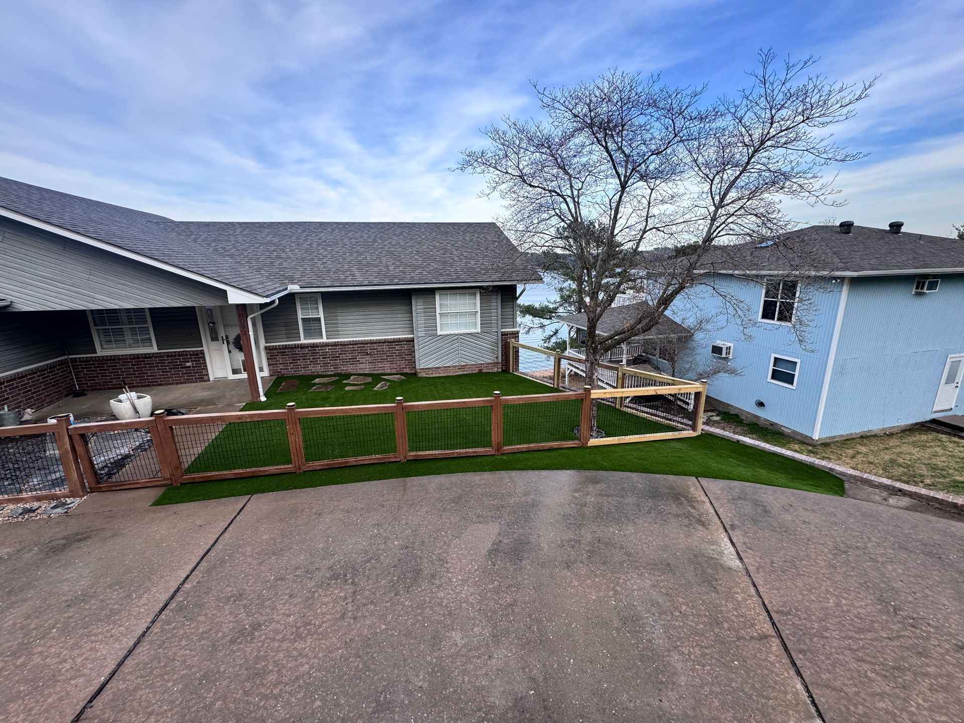 A house with brown roof, a green lawn, and a wooden fence with a blue sky background.
