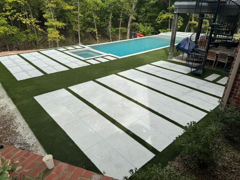 Backyard with pool, pavers, and artificial turf. White pavers set in green turf, a hot tub, and a spiral staircase are visible.