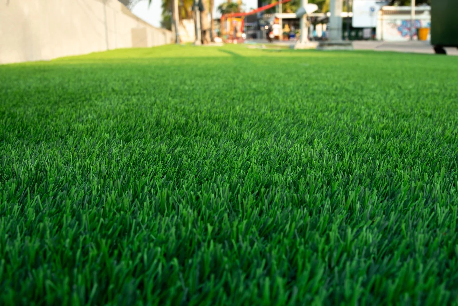 Green artificial turf, low-angle view with a concrete wall and buildings in the background.