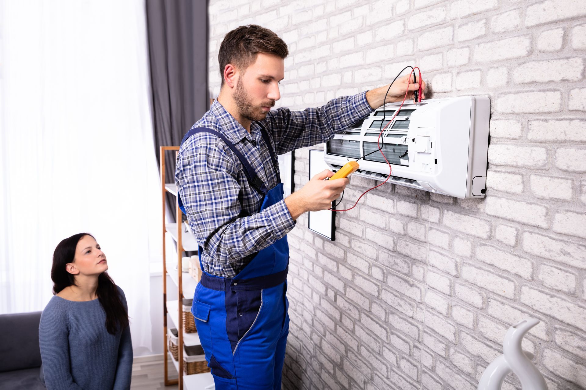 Technician performing AC repairs while examining an air conditioner with a digital multimeter.