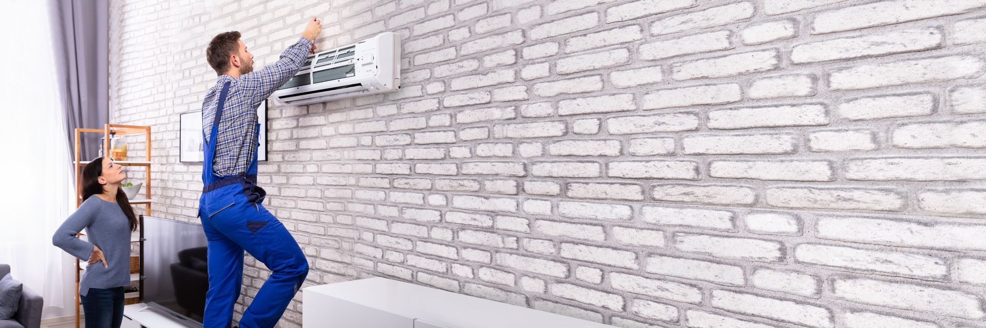 A technician wearing blue overalls is conducting AC repairs on an air conditioner with expert care. A technician wearing blue overalls is conducting AC repairs on an air conditioner with expert care.