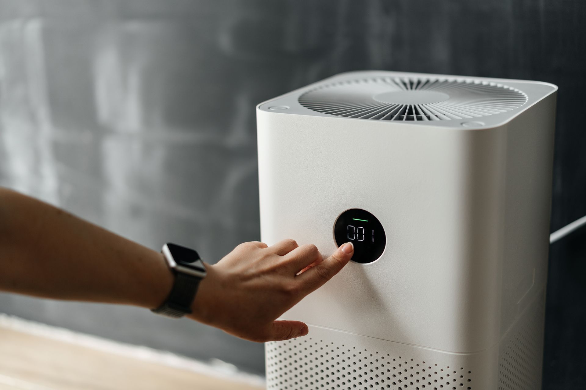 Woman's hand presses the touch screen button to start an air purifier in her apartment.