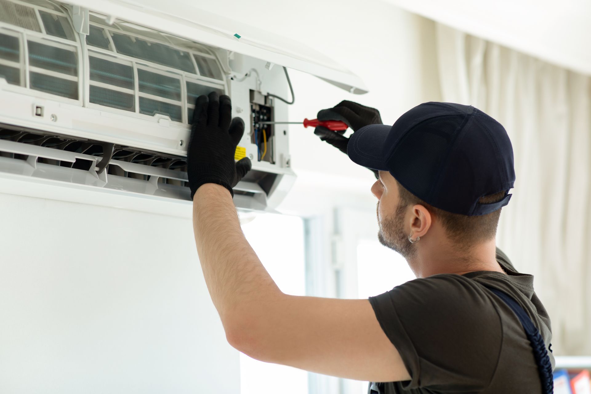 Technician fixing AC unit with screwdriver indoors.