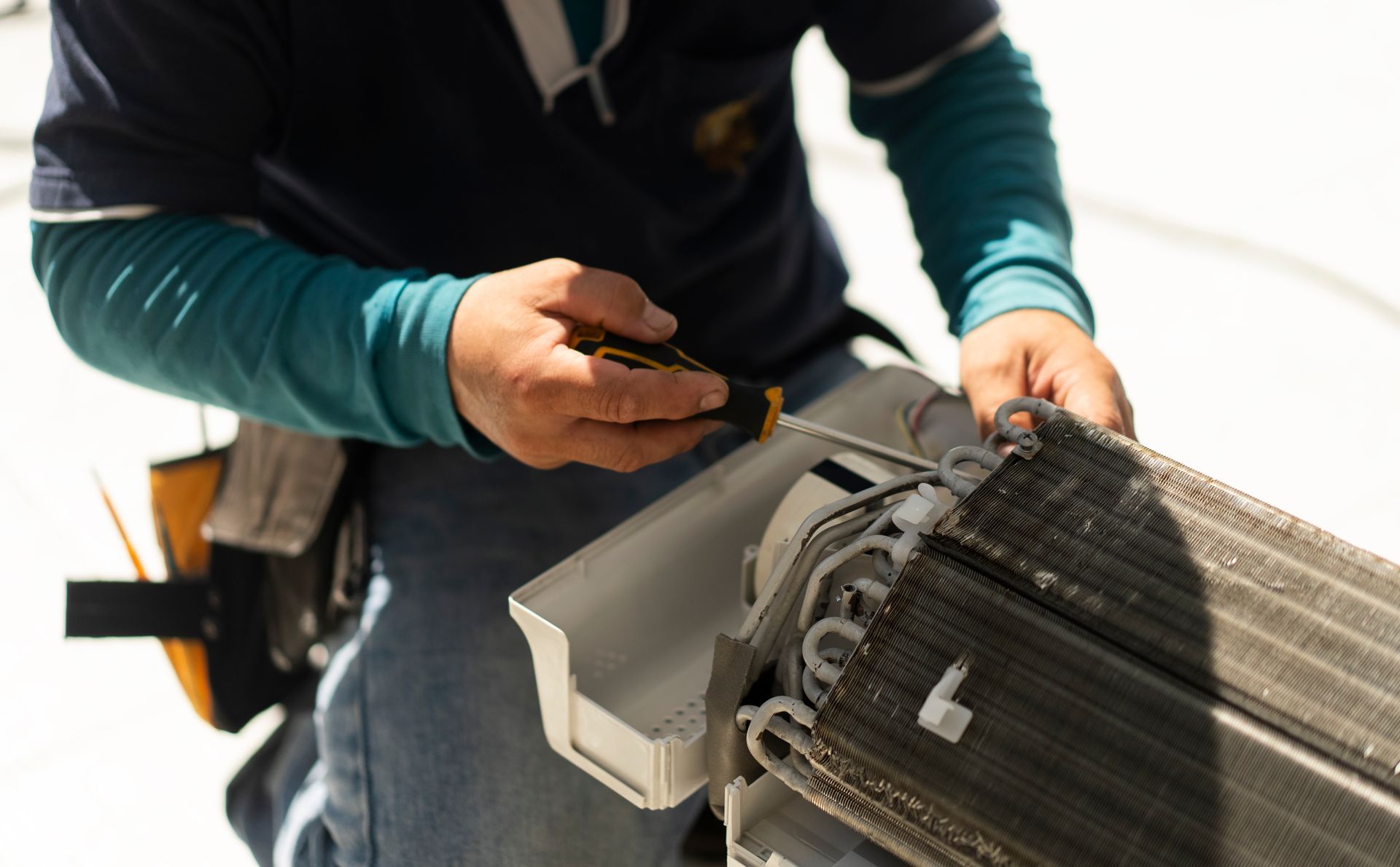 Technician performing air conditioning repair using a screwdriver on AC unit coil.