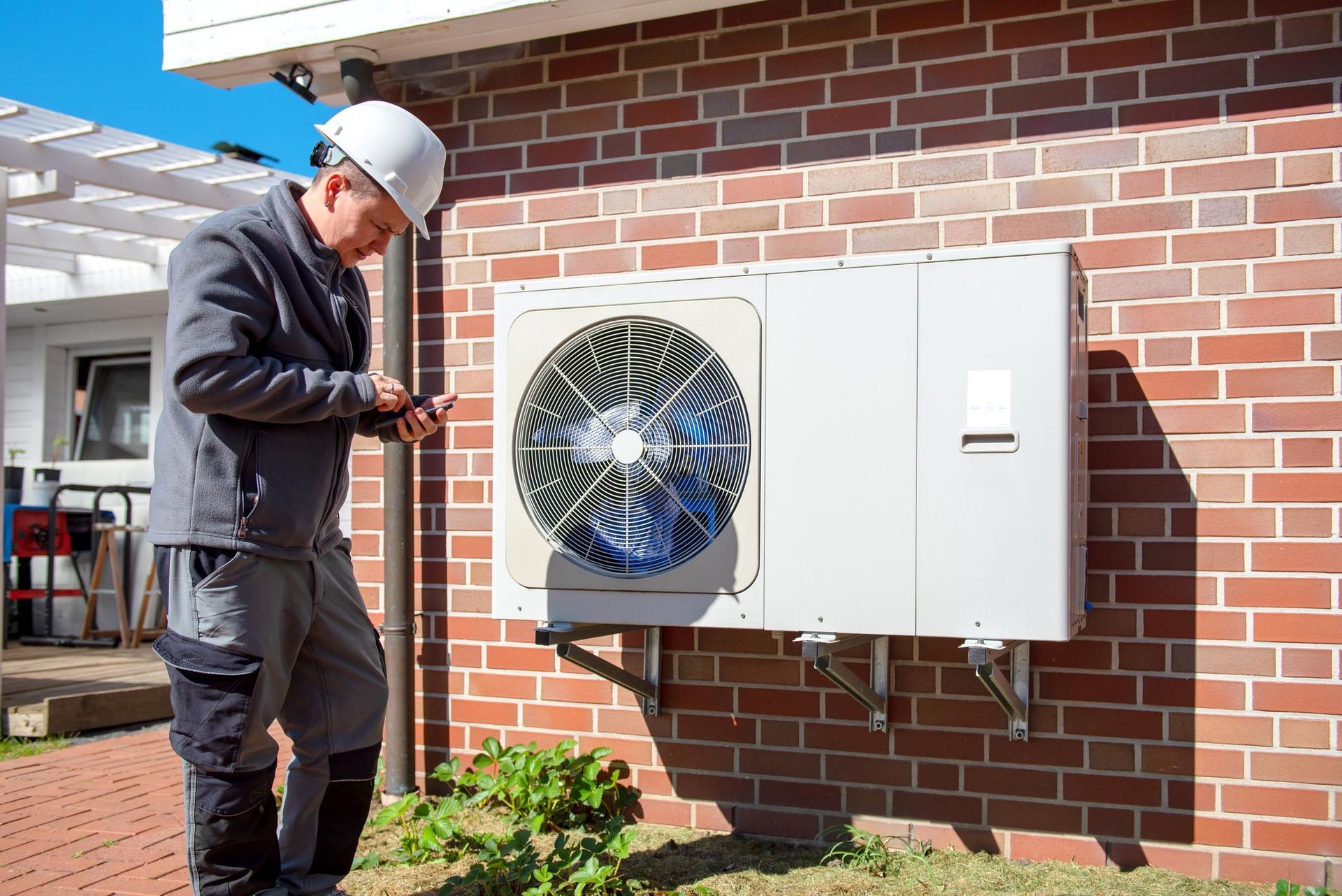 HVAC technician inspecting outdoor AC unit on brick building using handheld device for maintenance.