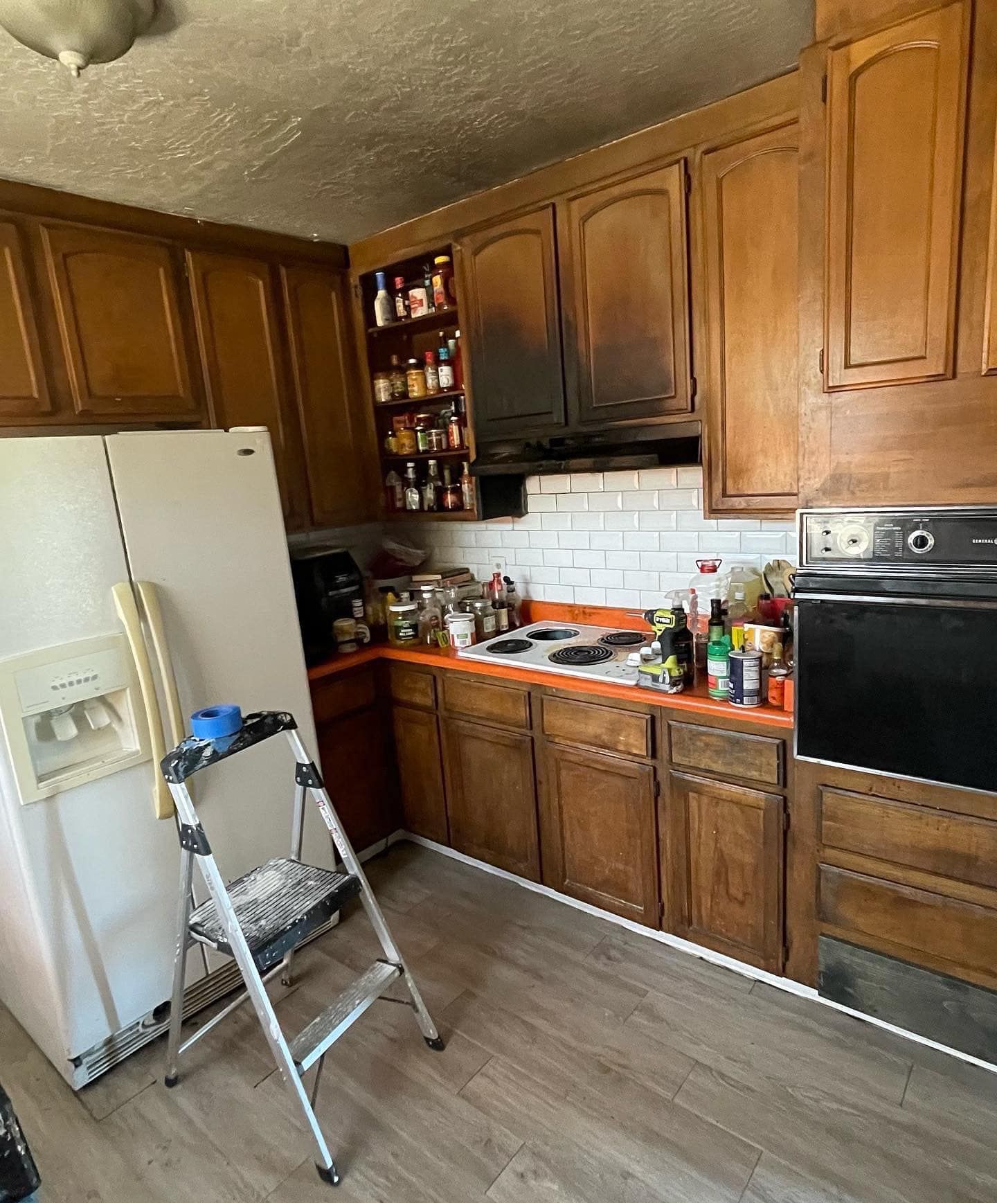 Kitchen with wooden cabinets, a white refrigerator, and a step ladder; evidence of fire damage.