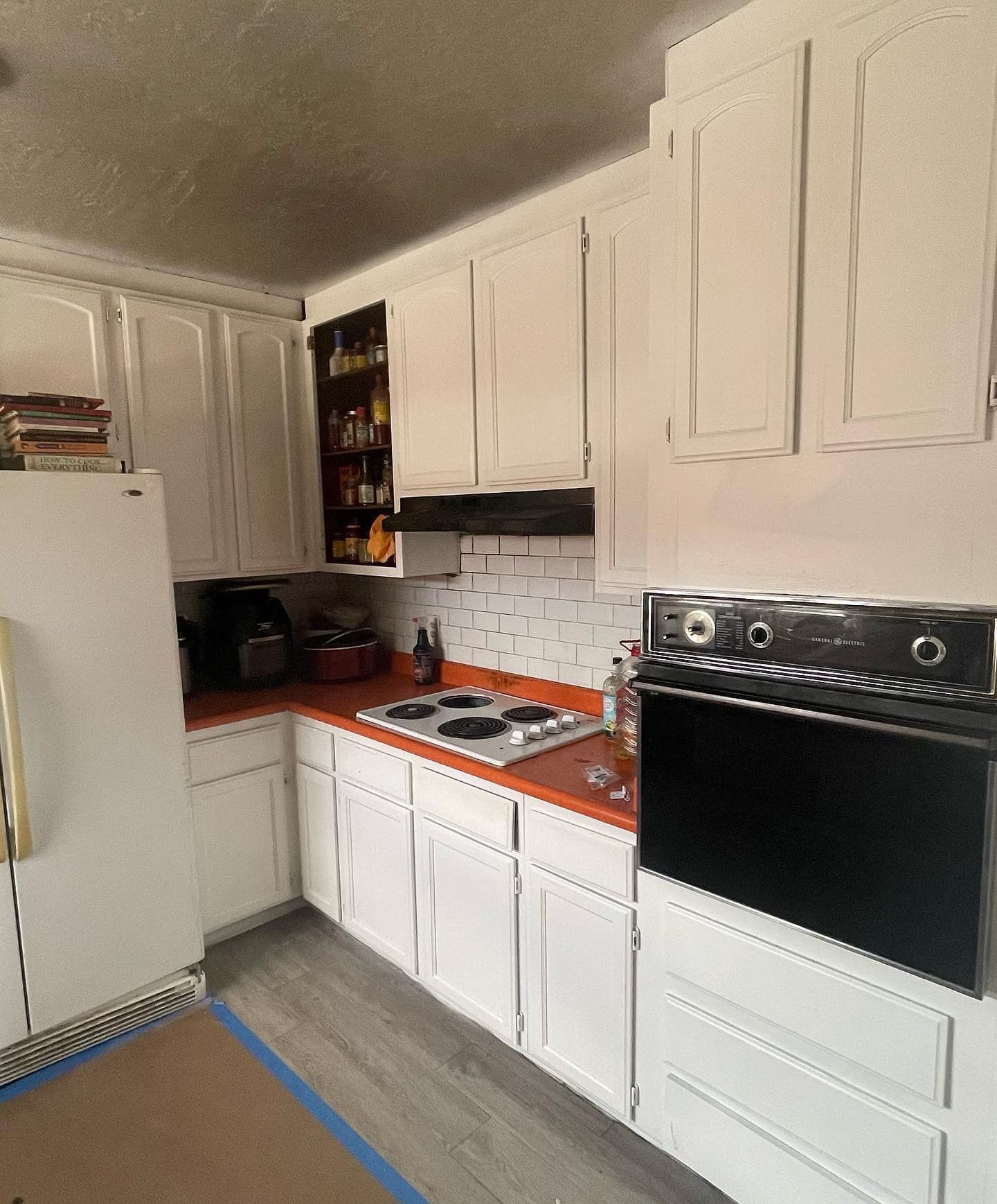 White kitchen cabinets, orange countertop, stove, oven, and refrigerator.