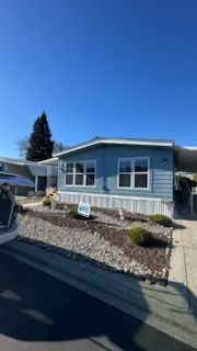 Blue mobile home with white trim, gravel landscaping, and a clear blue sky.