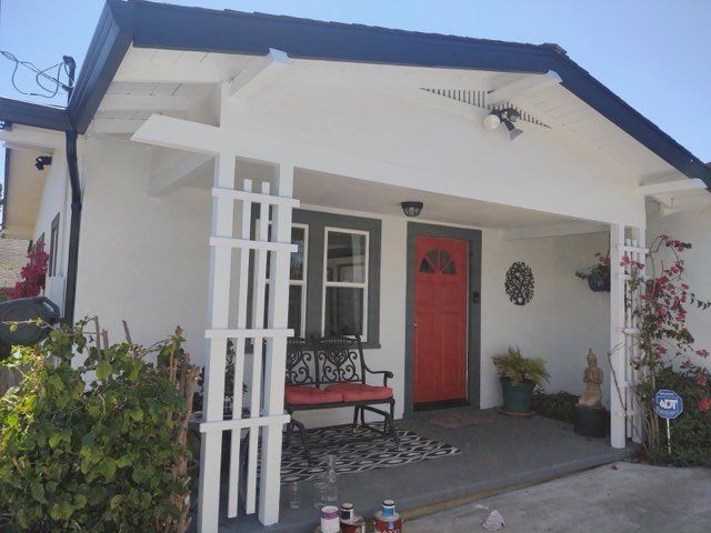 White house with a red door, black roof, and decorative white lattice.