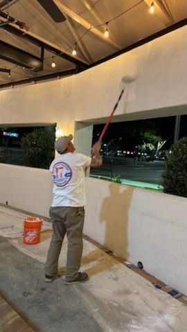 Man painting white wall outdoors with roller and extension pole.