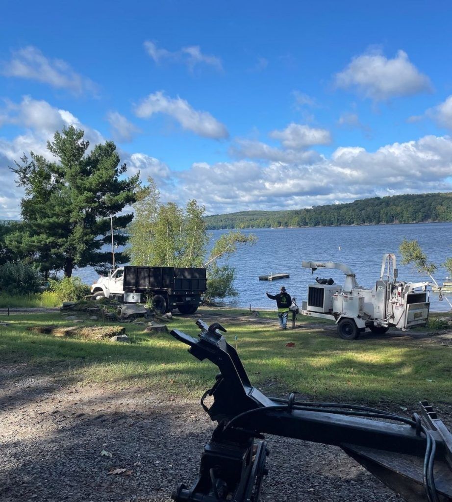 A man is standing on the shore of a lake next to a trailer.