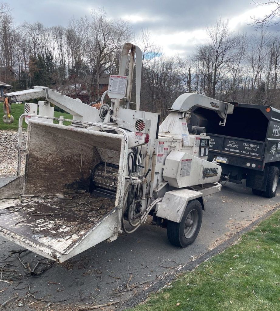 A tree chipper is sitting on the side of the road next to a dump truck.