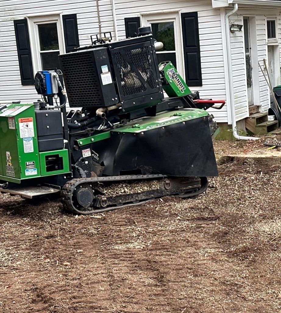 A green and black machine is sitting in the dirt in front of a house.