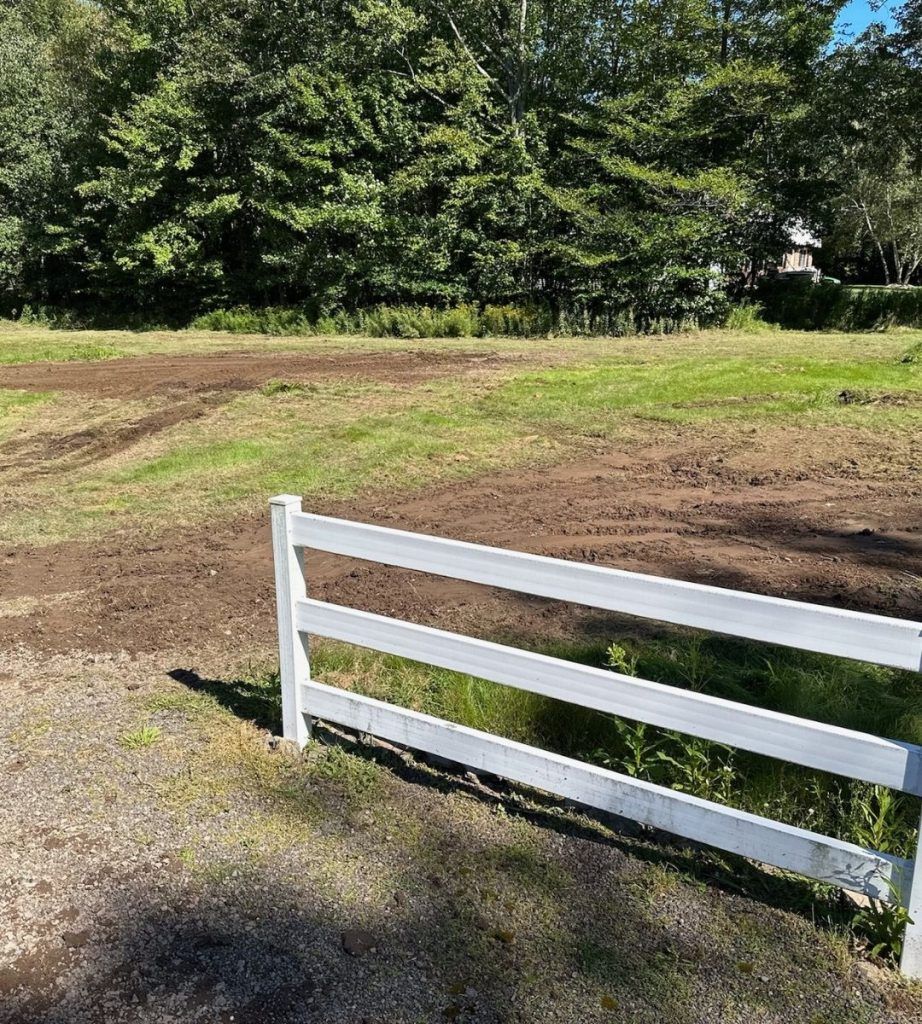 A white fence surrounds a grassy field with trees in the background.