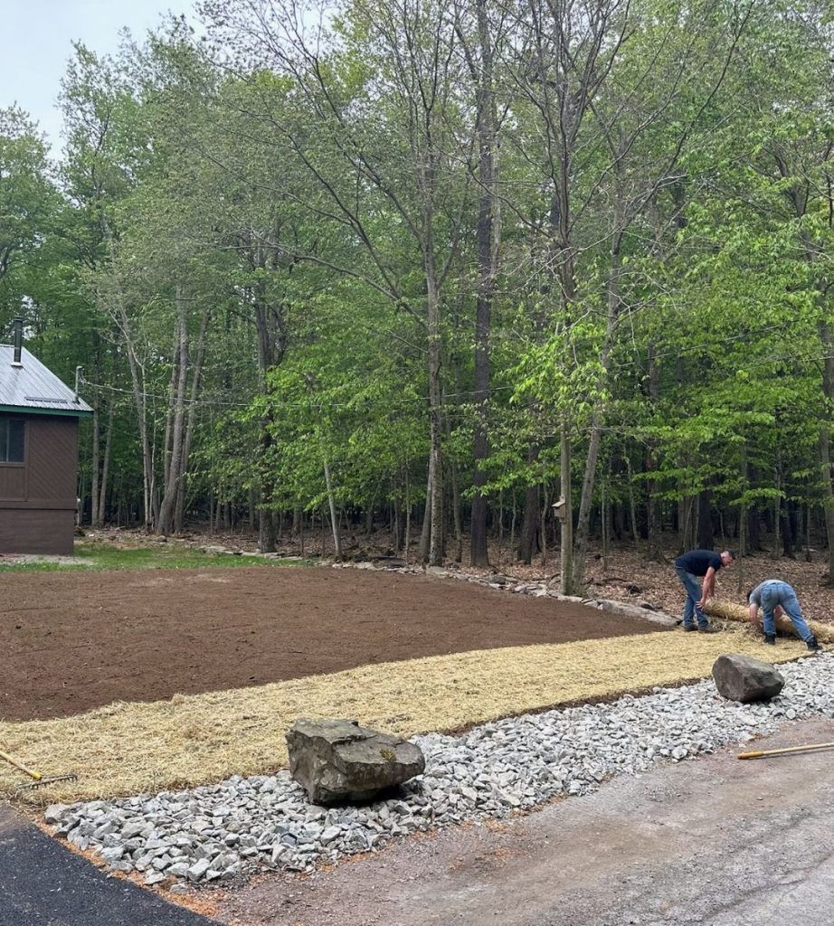 A man is working on a gravel driveway next to a house in the woods.