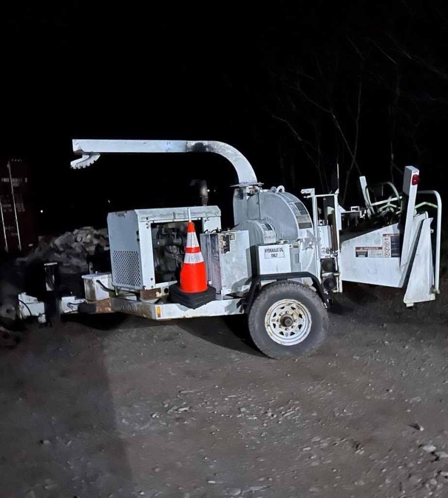 A tree chipper is parked on the side of the road at night.