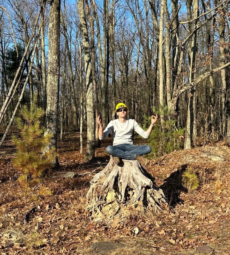 A woman is sitting on a tree stump in the woods.