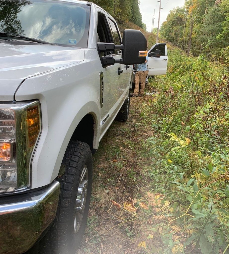 A white truck is parked on a dirt road in the woods.