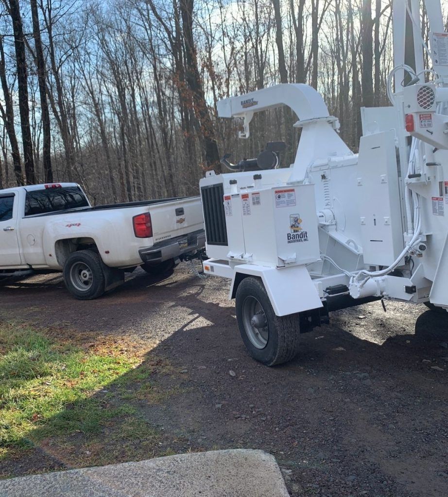 A white truck is towing a white tree chipper on a trailer.