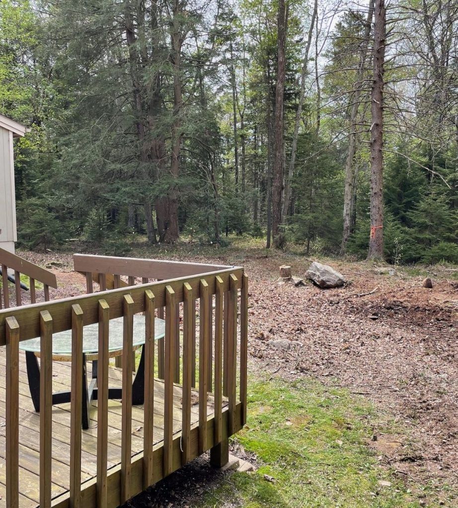 A wooden deck with a table and chairs in the middle of a forest.