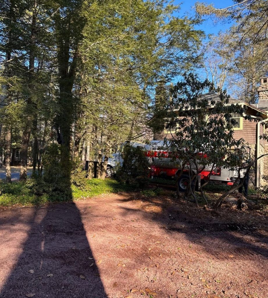 A red truck is parked on the side of a dirt road next to a house.