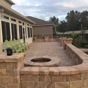 Brick patio with built-in fire pit, surrounded by low brick walls, adjacent to a home.