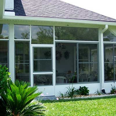 White framed sunroom with glass windows and a door, next to green grass and plants.