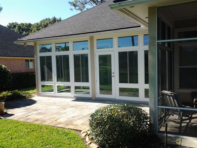 Sunroom with white trim and large windows, adjacent to a patio with brick pavers.