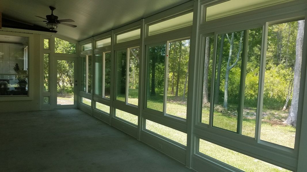 Sunroom with large windows overlooking a green forest. Light fills the room.