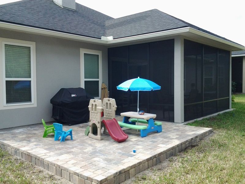 Patio with kids' play area, grill, and screened porch against a gray house.