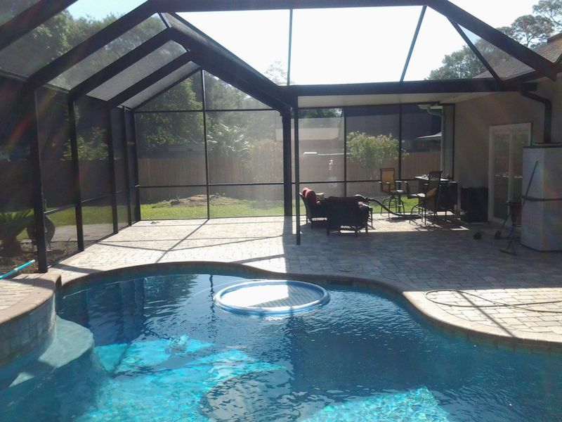 Screened-in pool enclosure with a pool, seating area, and lush backyard.