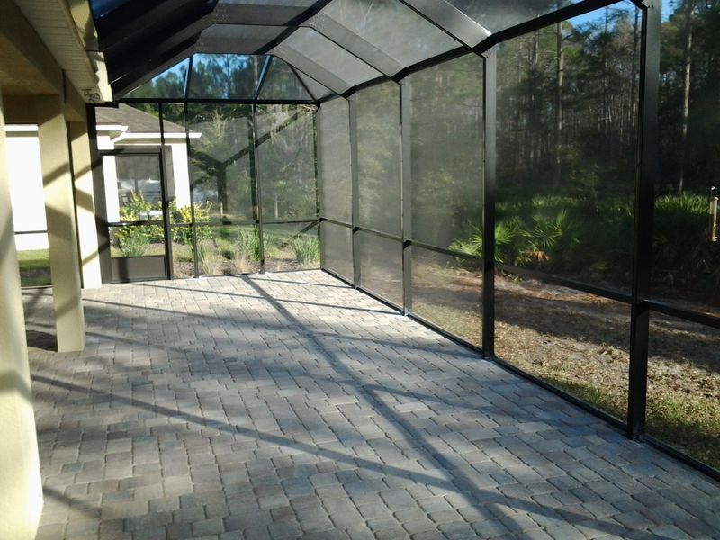 Screened-in patio with gray brick floor and black frame, overlooking a wooded backyard.