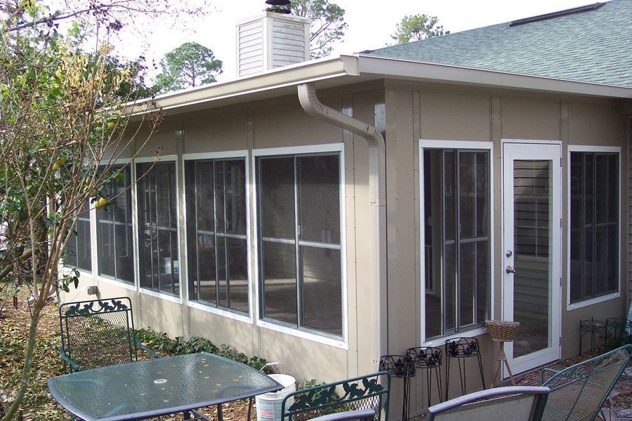 A sunroom with screened windows and a door, attached to a house with beige siding, overlooking a patio.