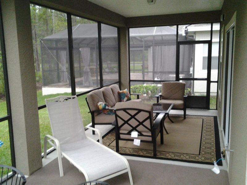 Screened porch with outdoor furniture including a sofa, chairs, and chaise lounge on a rug.