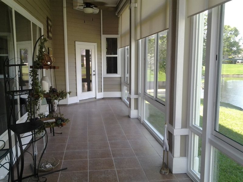 Enclosed porch with tiled floor and large windows overlooking a body of water.